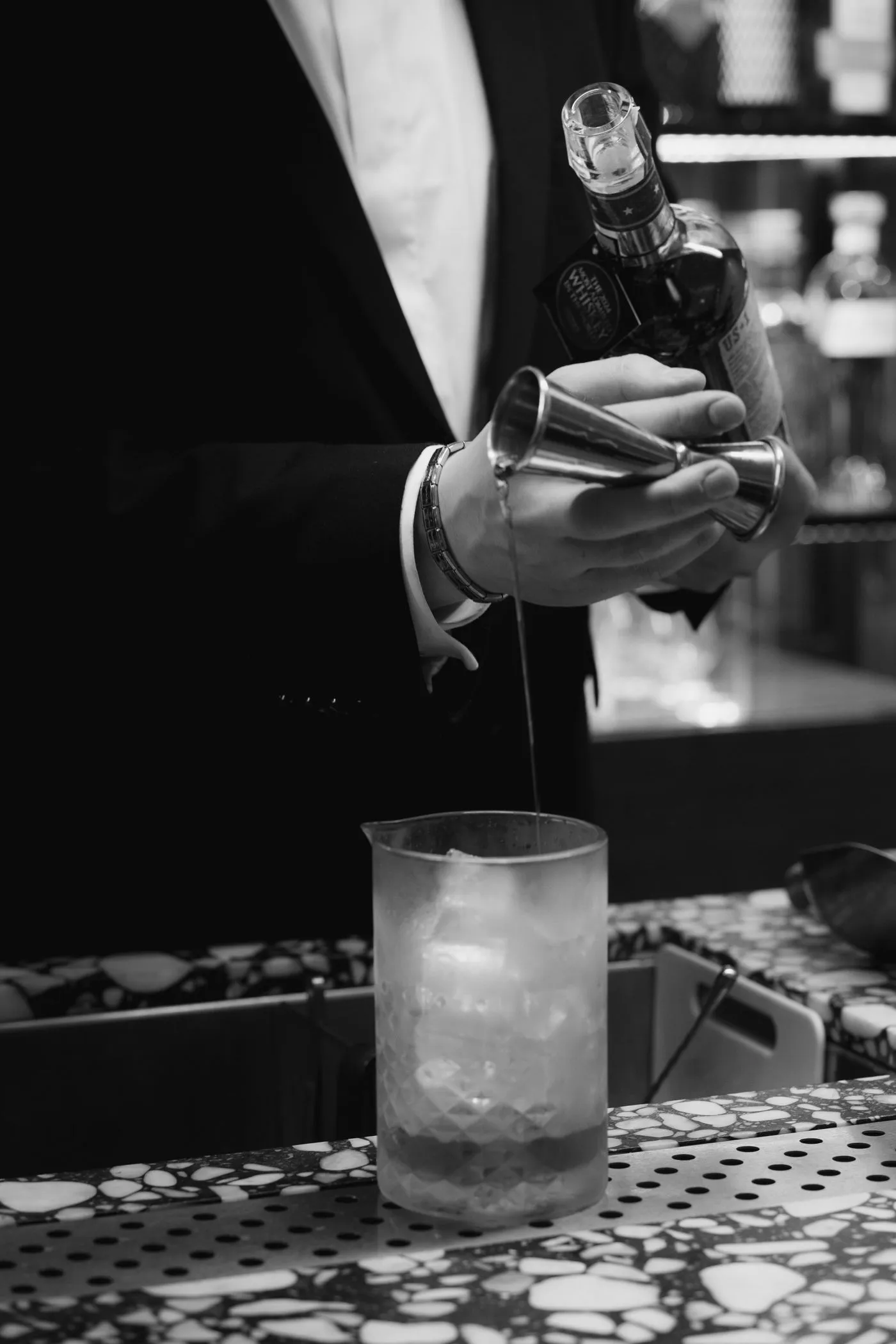 A bartender's hands straining a freshly shaken cocktail behind the bar