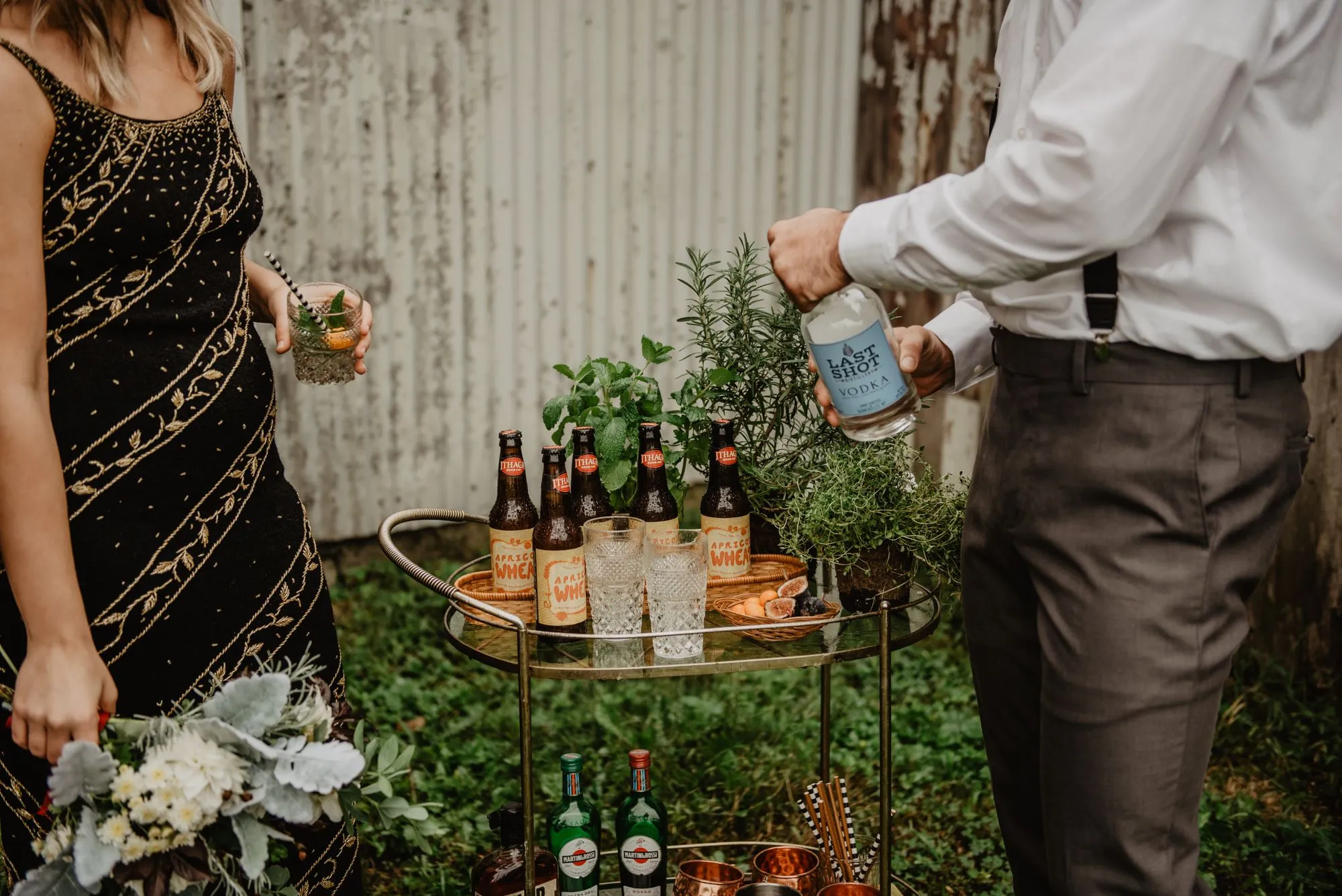 Two people in evening dress mixing cocktails at an outdoor drinks table lit by candlelight
