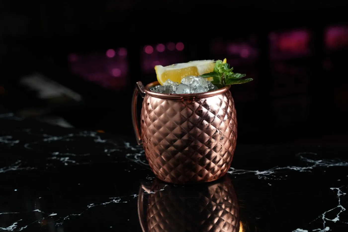 A garnished drink in a hammered copper cup resting on a dark marble bar counter