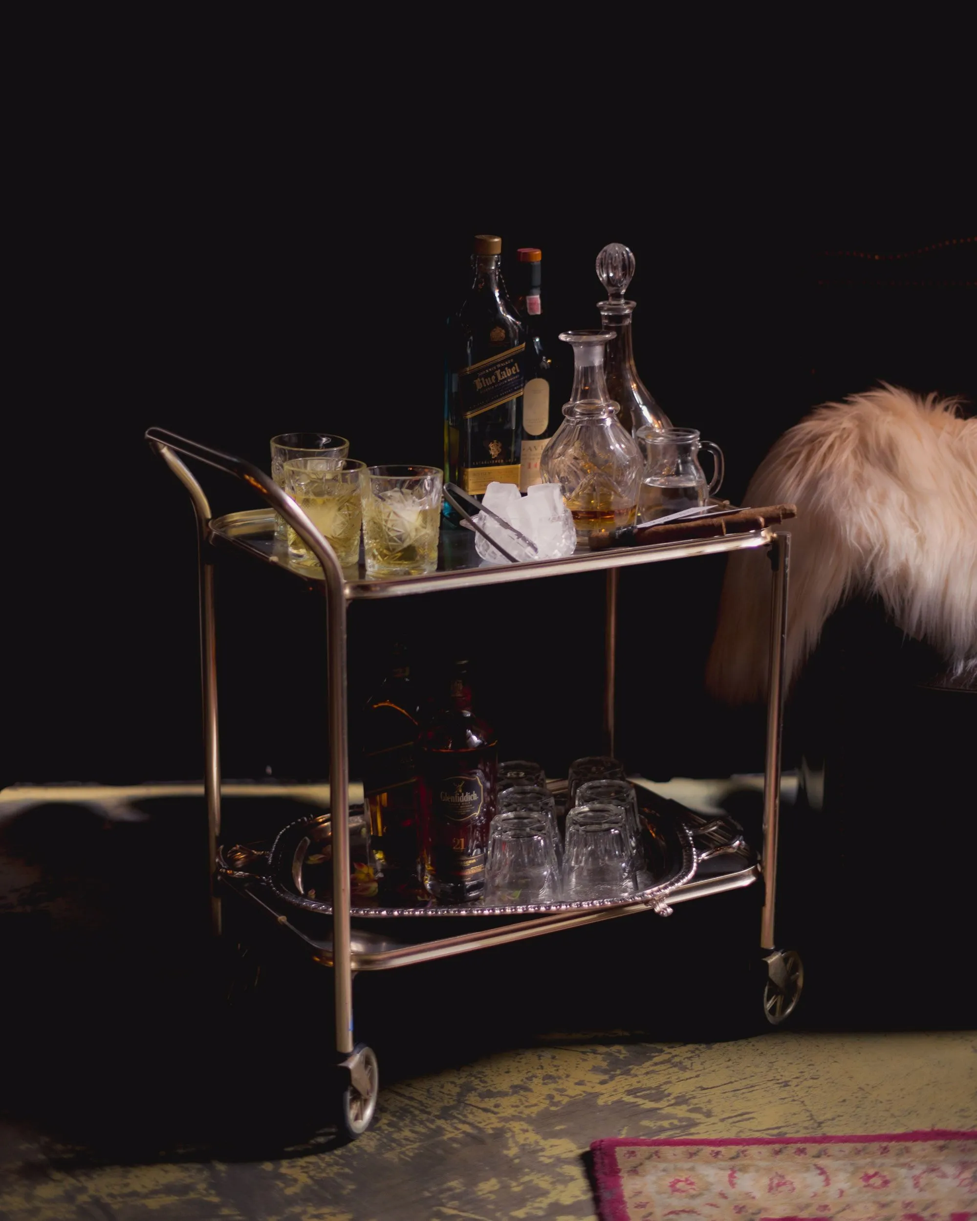 A brass drinks trolley set with crystal decanters and glassware against a dark interior