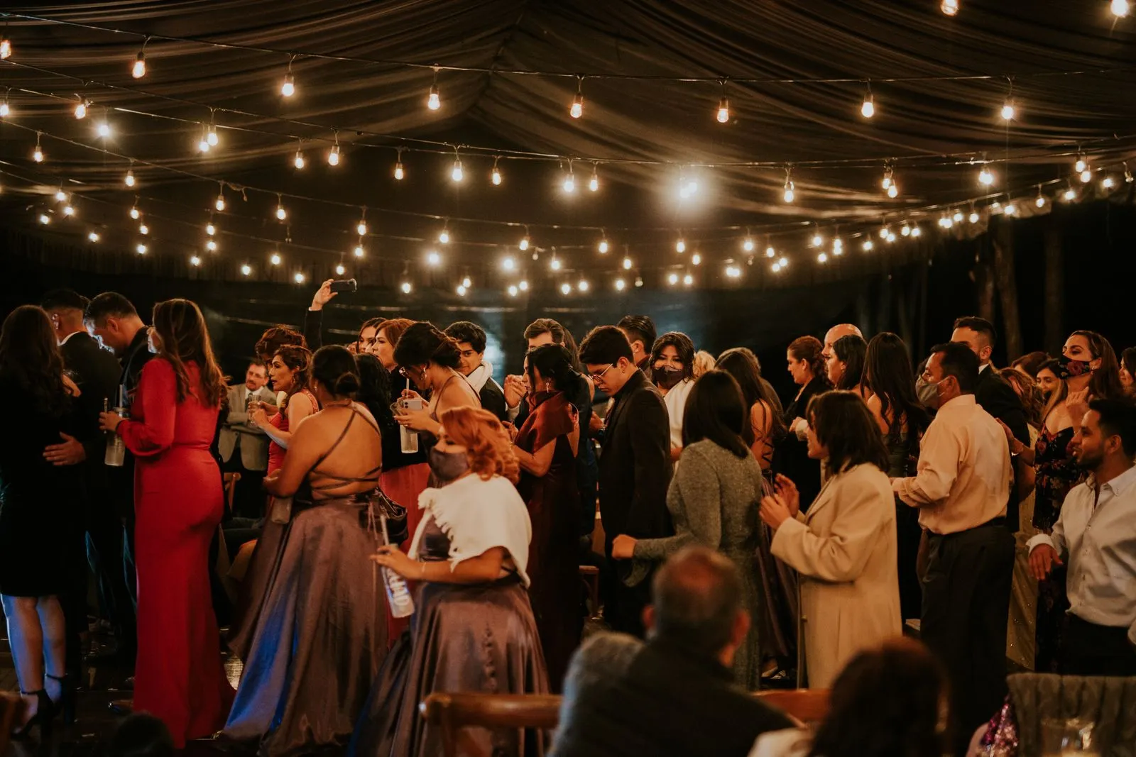 A large crowd of guests gathered under strung lights at an evening event