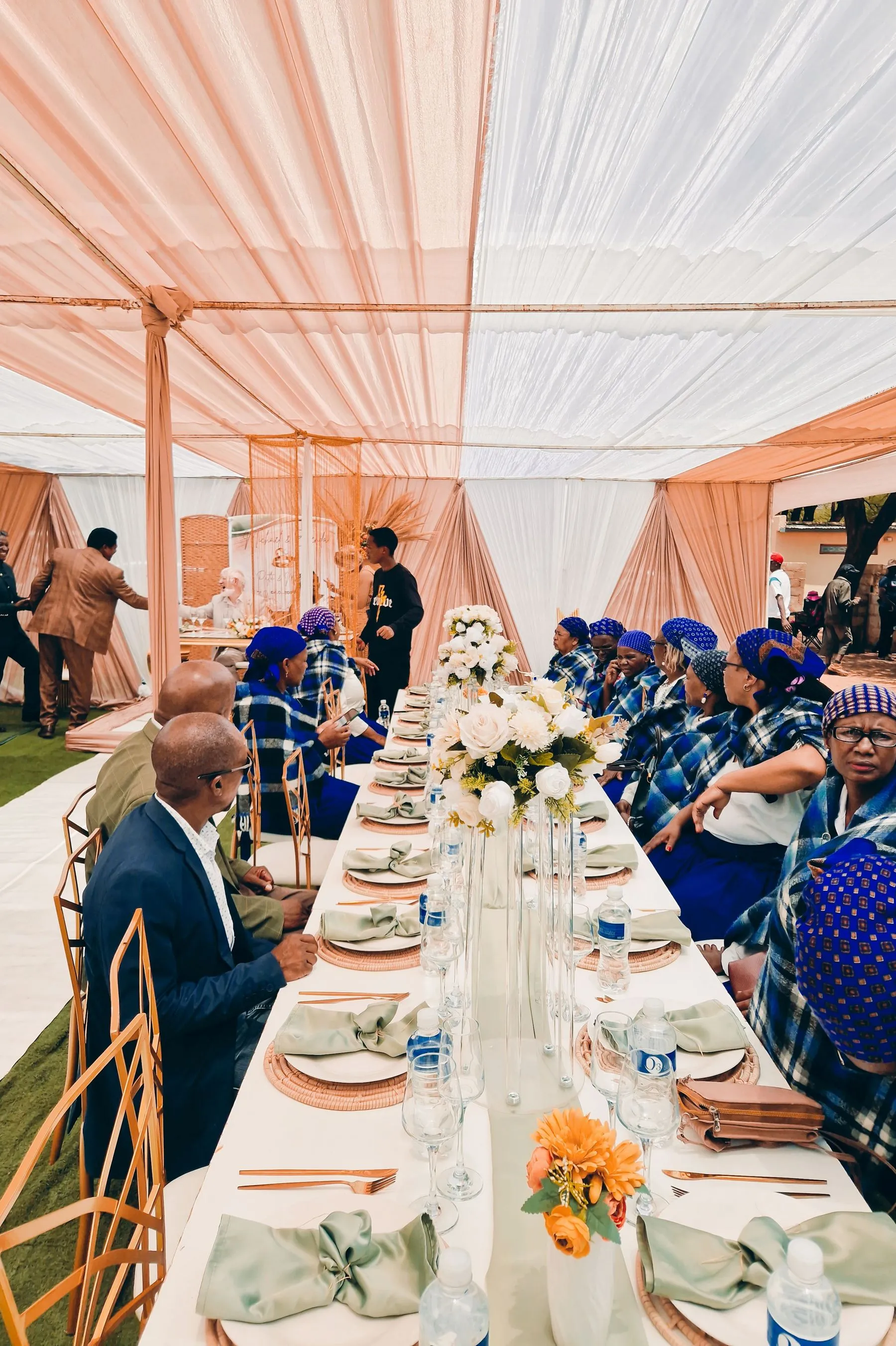 Guests in traditional attire seated at a dressed outdoor reception under a marquee