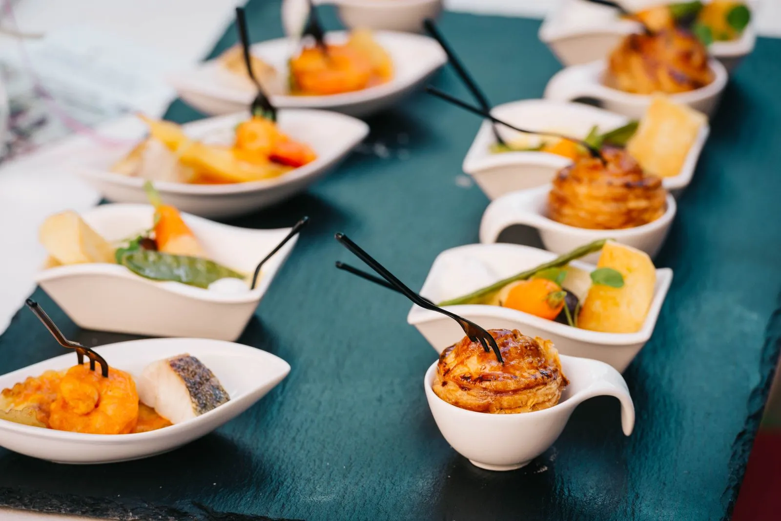 Assorted canapés arranged in white spoons across a dark slate serving tray