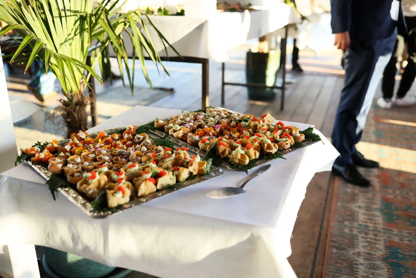 A catering table of assorted appetisers at an event with guests in formal dress behind it