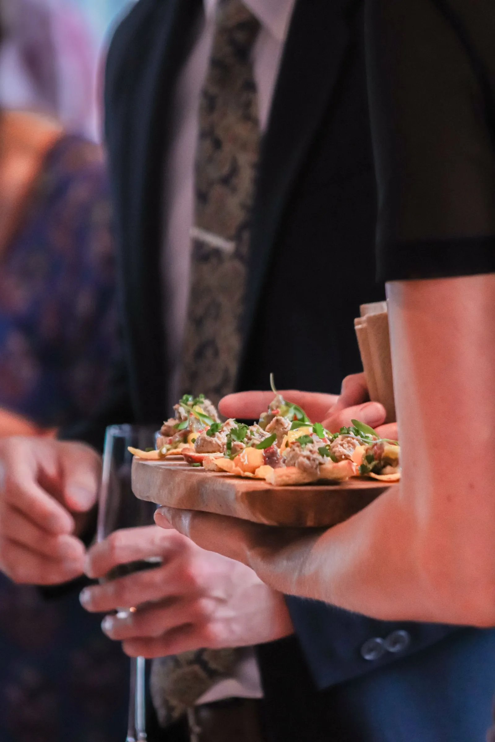 A server presenting a wooden tray of plated appetisers to guests at a formal event