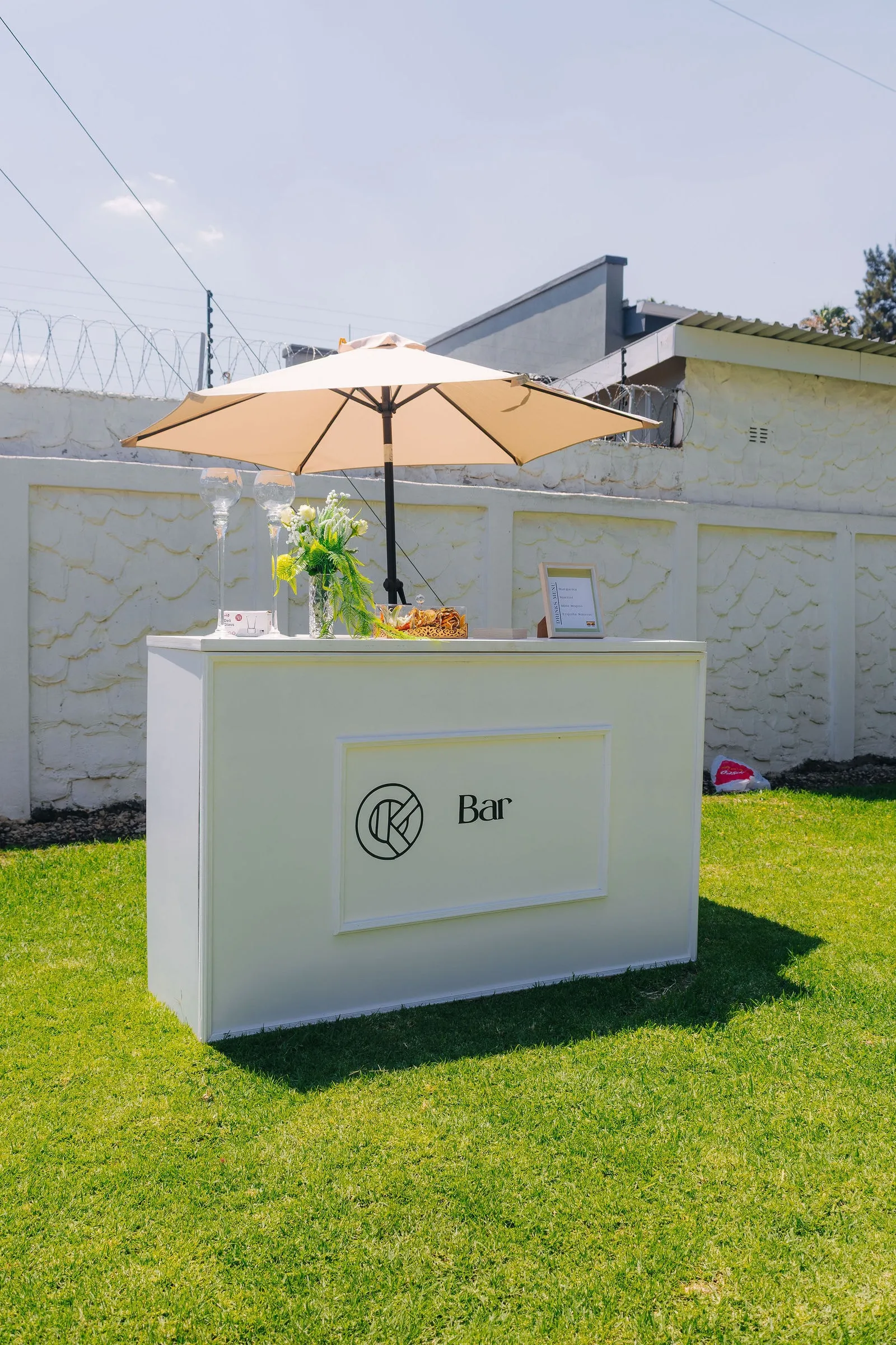 The white KaizenCo Bar cart styled with flowers and glassware beneath a parasol at the launch event