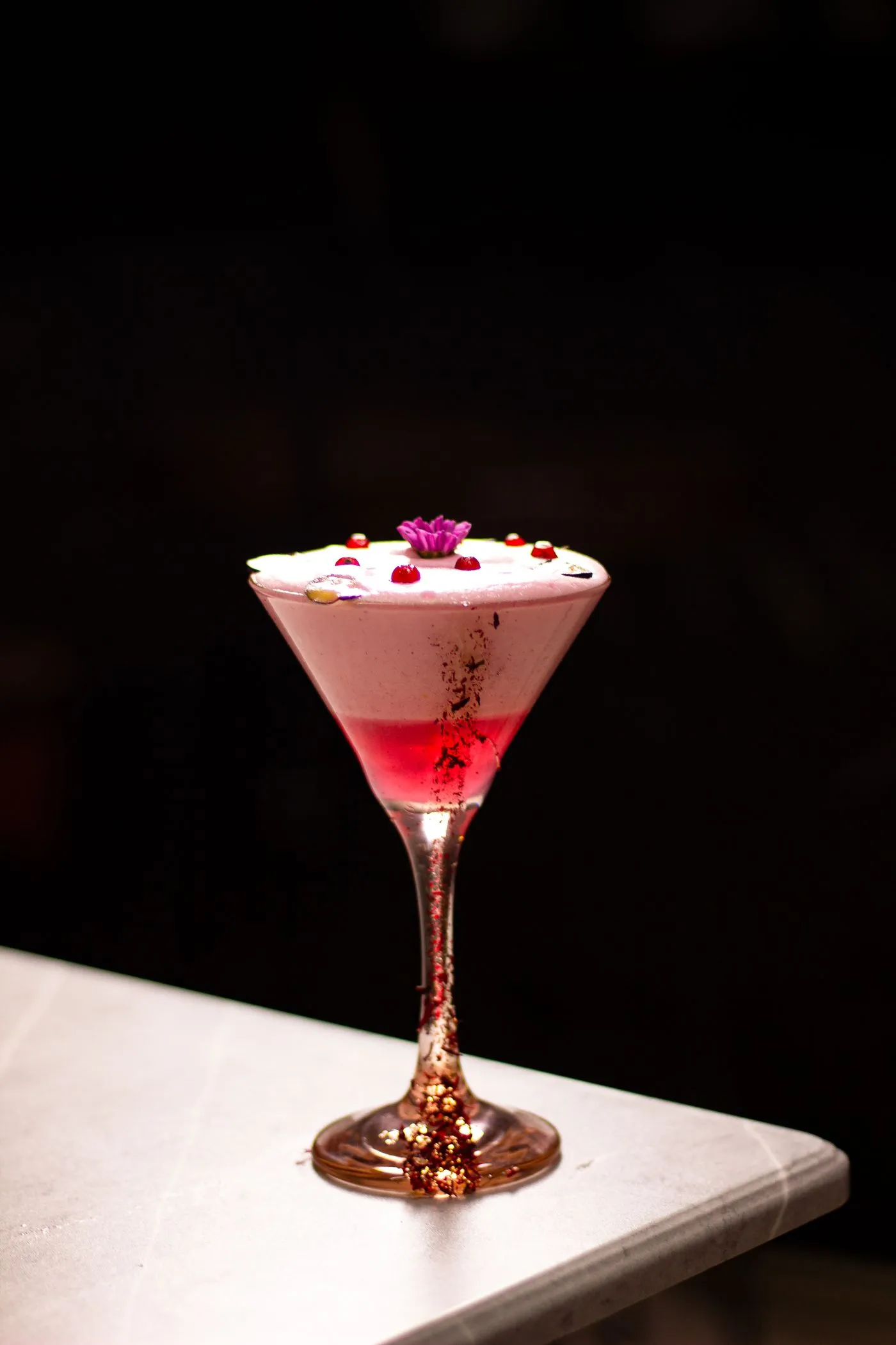 A layered alcohol-free drink in a stemmed glass finished with a dried flower garnish