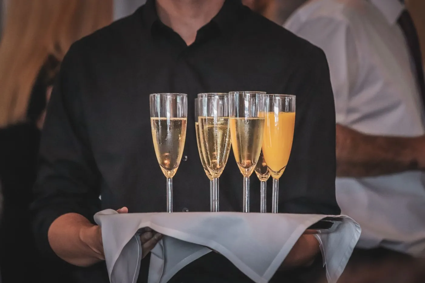 A member of the service team in black holding a tray of filled sparkling wine glasses